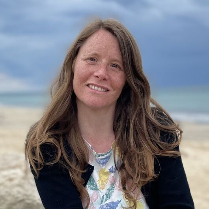 Photo de moi assise en tailleur avec en fond la plage et un beau ciel bleu